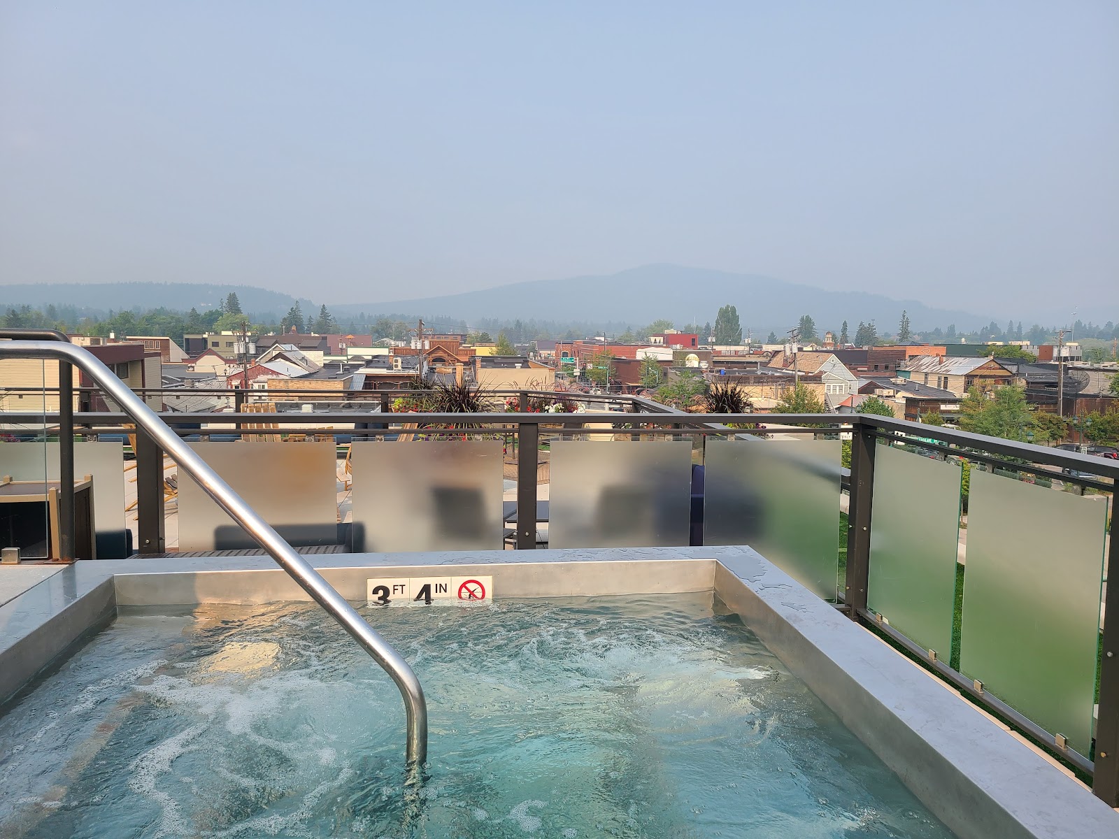 Rooftop hot tub on a hotel terrace overlooking Whitefish with the distant Glacier National Park peaks in the background.