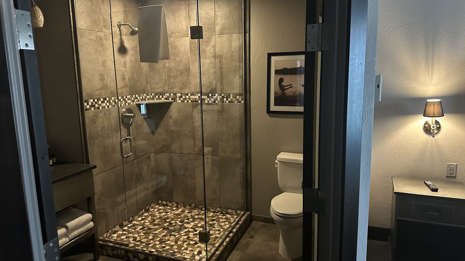 Hotel bathroom in Glacier National Park lodging with glass-enclosed shower, tiled walls, and pebble floor.
