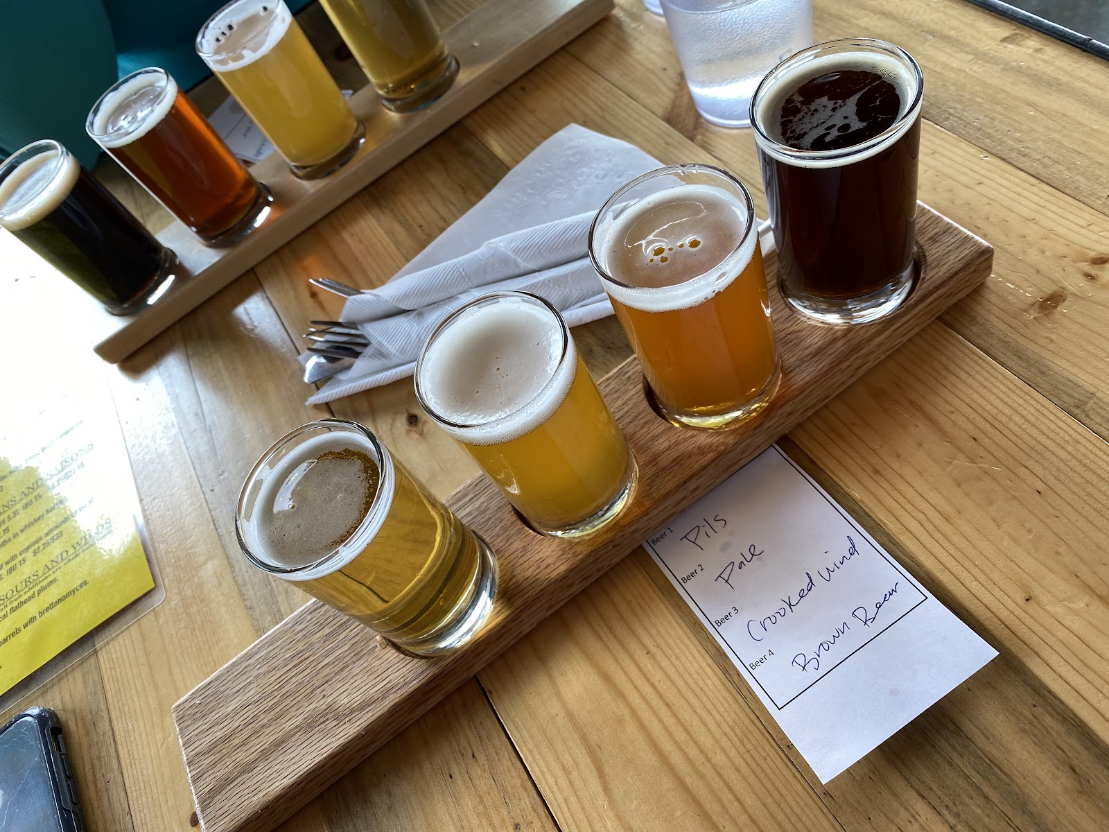 Beer flight tasting at Backslope Brewing inside Glacier National Park, showcasing multiple small pours on a wooden paddle.