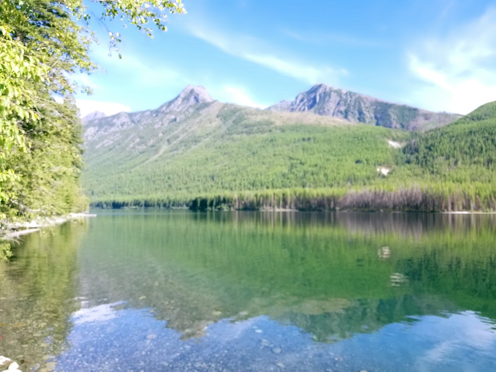 Emerald glacier-fed lake in Glacier National Park with forested shores and rugged mountains reflected in calm water.