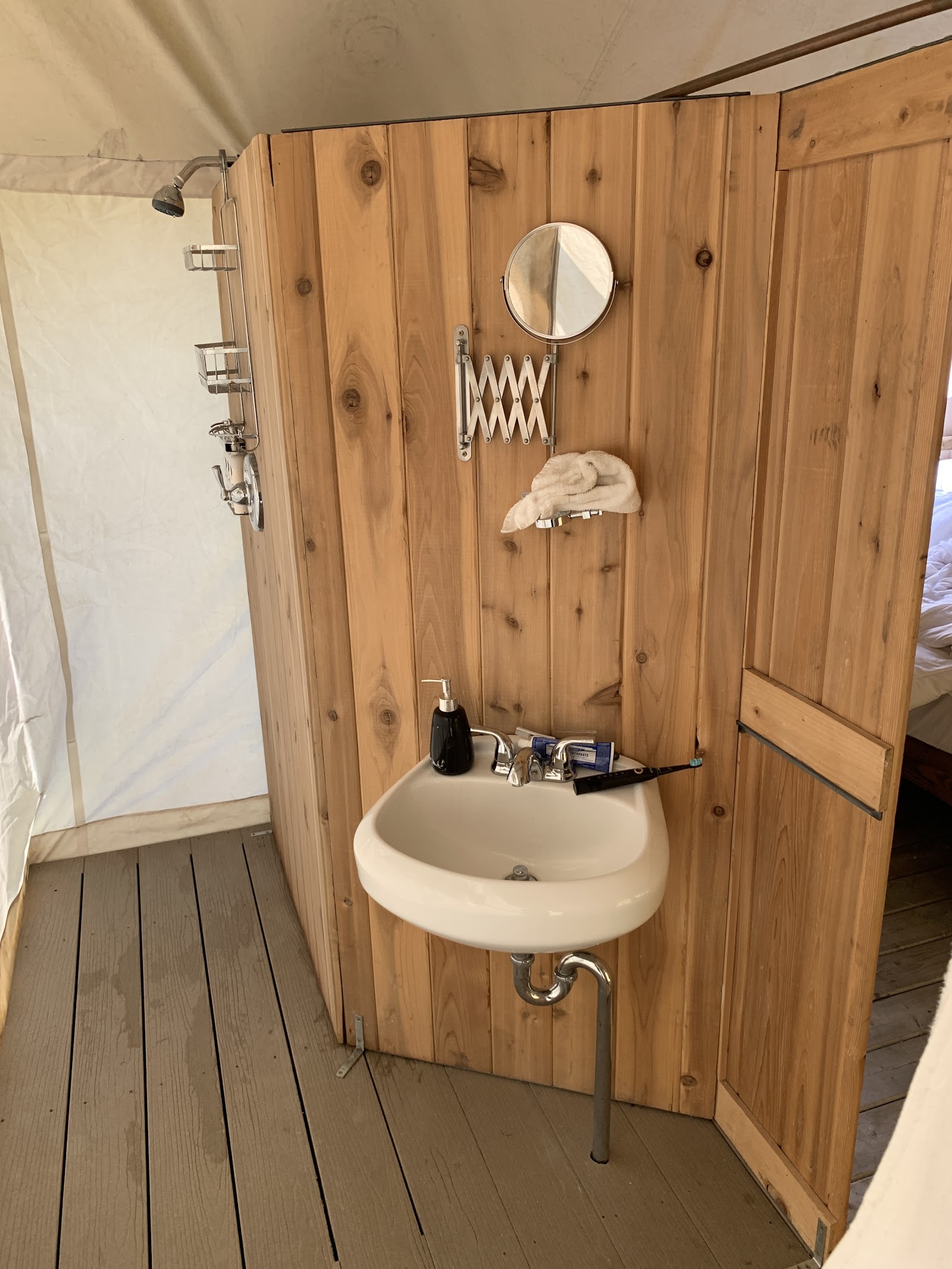 Rustic wooden bathroom in Glacier National Park tent lodge, white sink, round mirror, towel, and shower area.