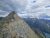 Numa Peak rises above rugged rock ridges in Glacier National Park, Montana, with distant mountains and a blue lake below.