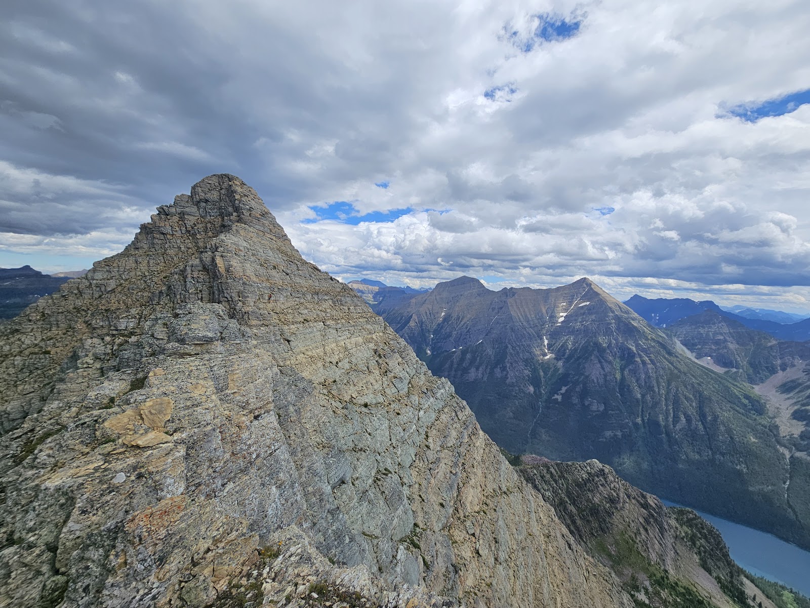 Numa Peak rises above rugged rock ridges in Glacier National Park, Montana, with distant mountains and a blue lake below.