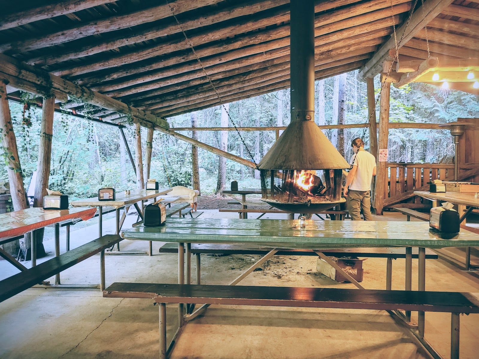 Glacier National Park rustic dining pavilion with a central fireplace and wooden benches inside a forested lodge.