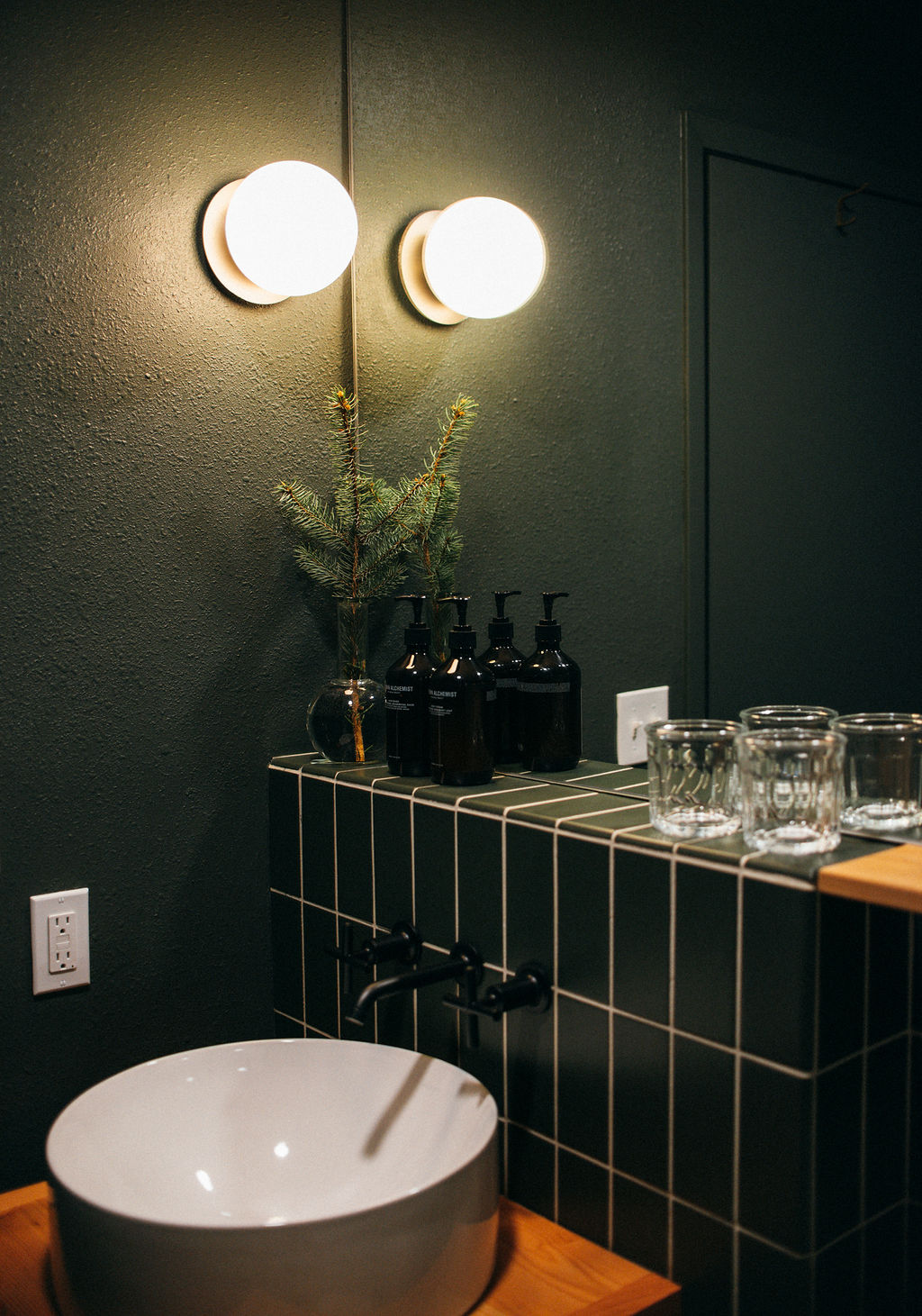 Cozy Glacier National Park lodging bathroom with a round sink, dark tile counter, and warm, dim lighting.