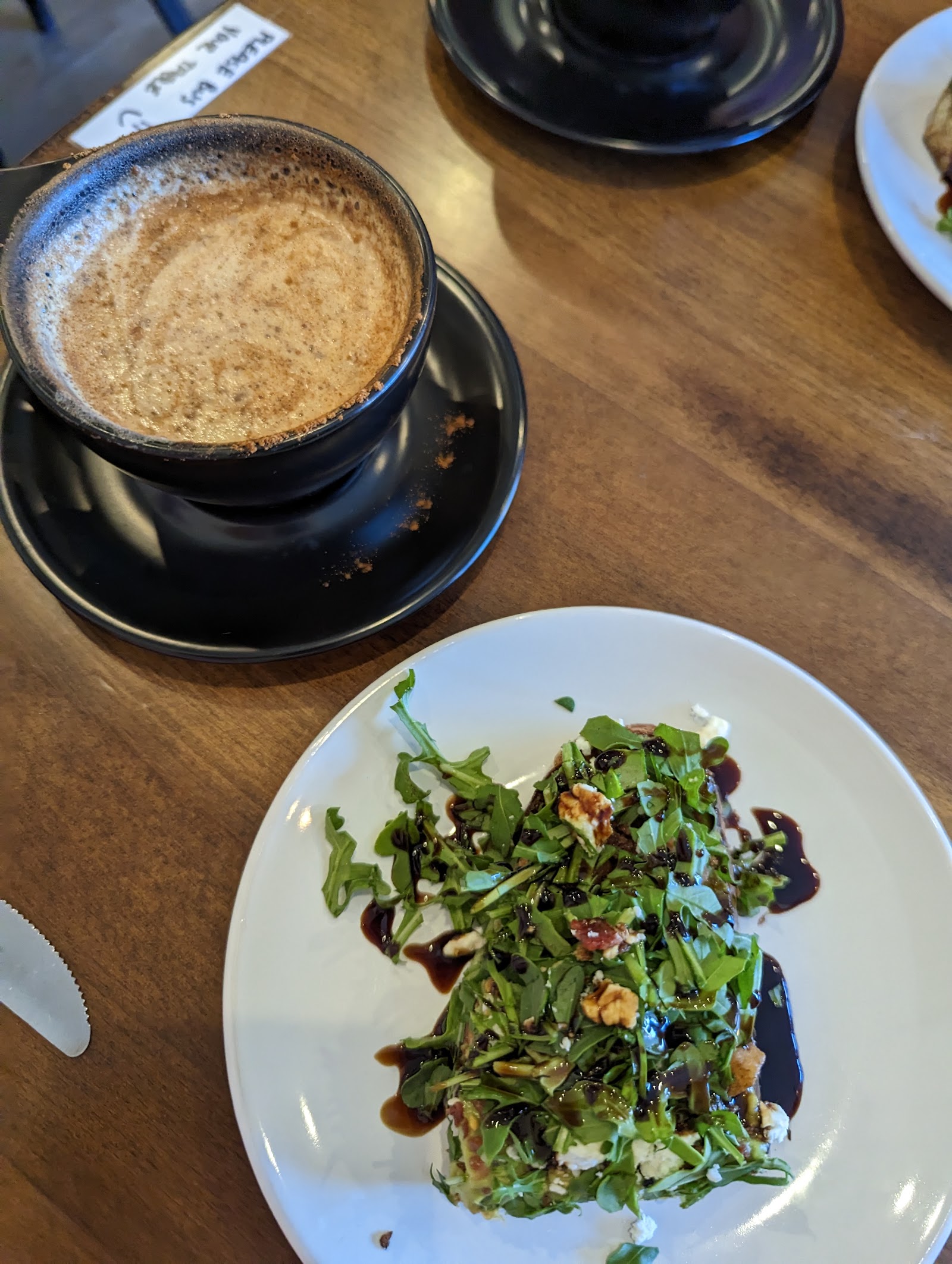 Indoor cafe scene at Glacier National Park featuring a frothy coffee cup and a fresh salad plate on a wooden table.