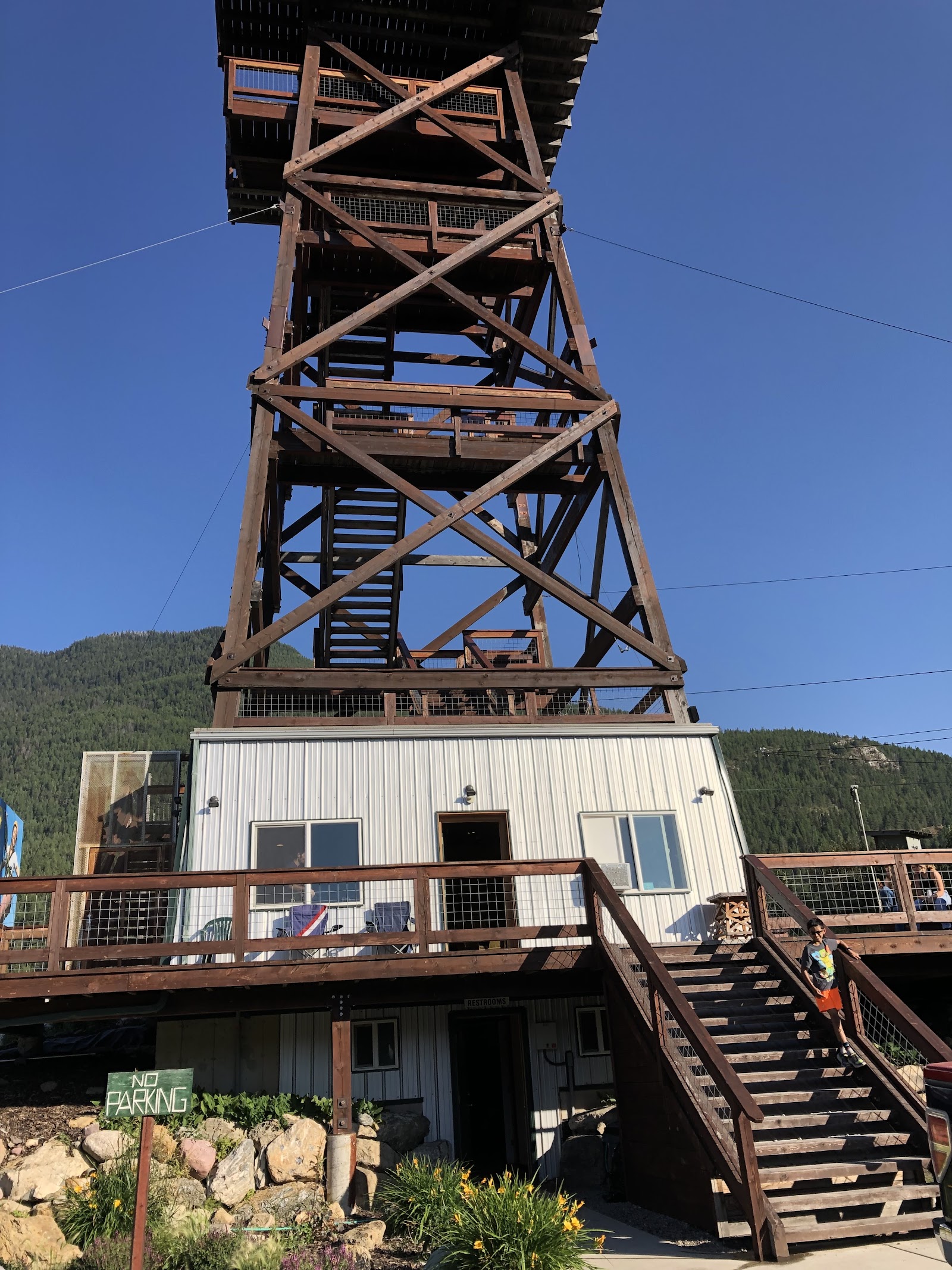 Glacier Ziplines tower rises above a wooden deck at Glacier National Park, with a clear blue sky overhead.