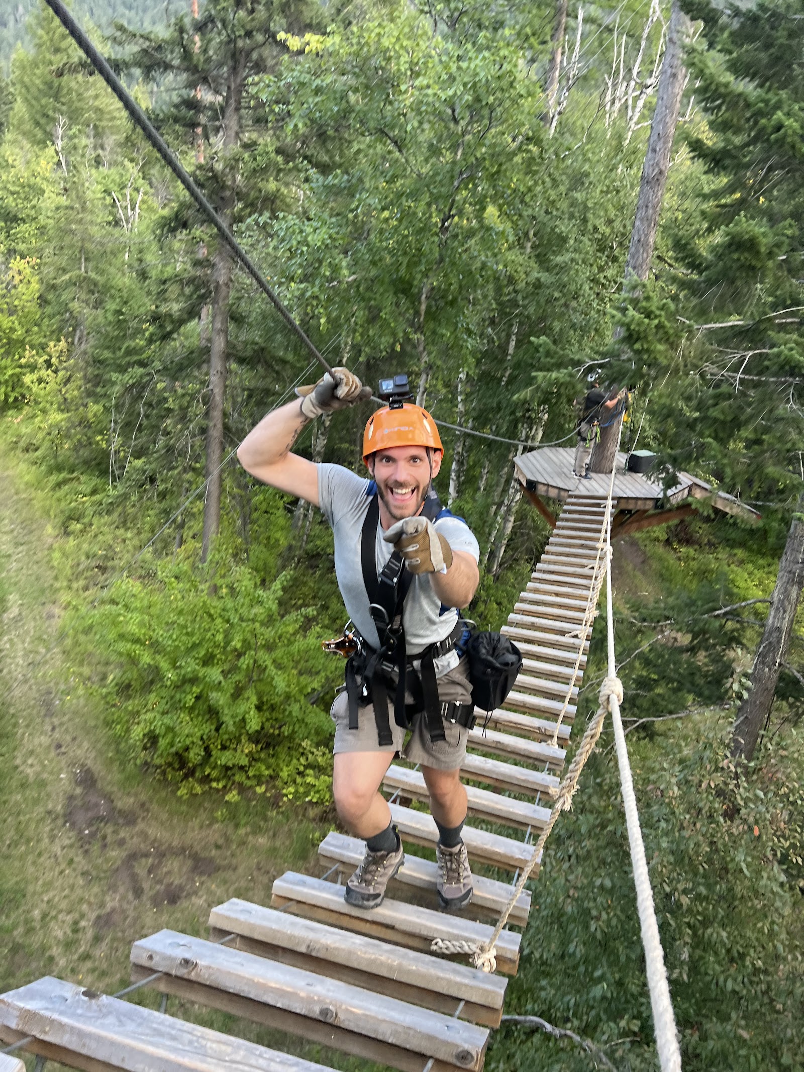 Glacier Ziplines rider on a forested zipline course in Glacier National Park, gripping ropes and smiling as he advances along the platform.