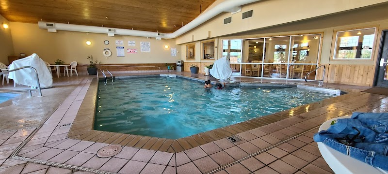 Indoor pool with turquoise water, tiled deck, wooden ceiling, and swimmers near large windows in Yellowstone National Park.