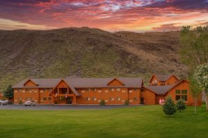 Wooden lodge exterior at sunset in Yellowstone National Park, with a grassy foreground and mountain backdrop.