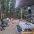 Campground scene in Glacier National Park with an RV, fire pit, and folding chairs around a small blaze.