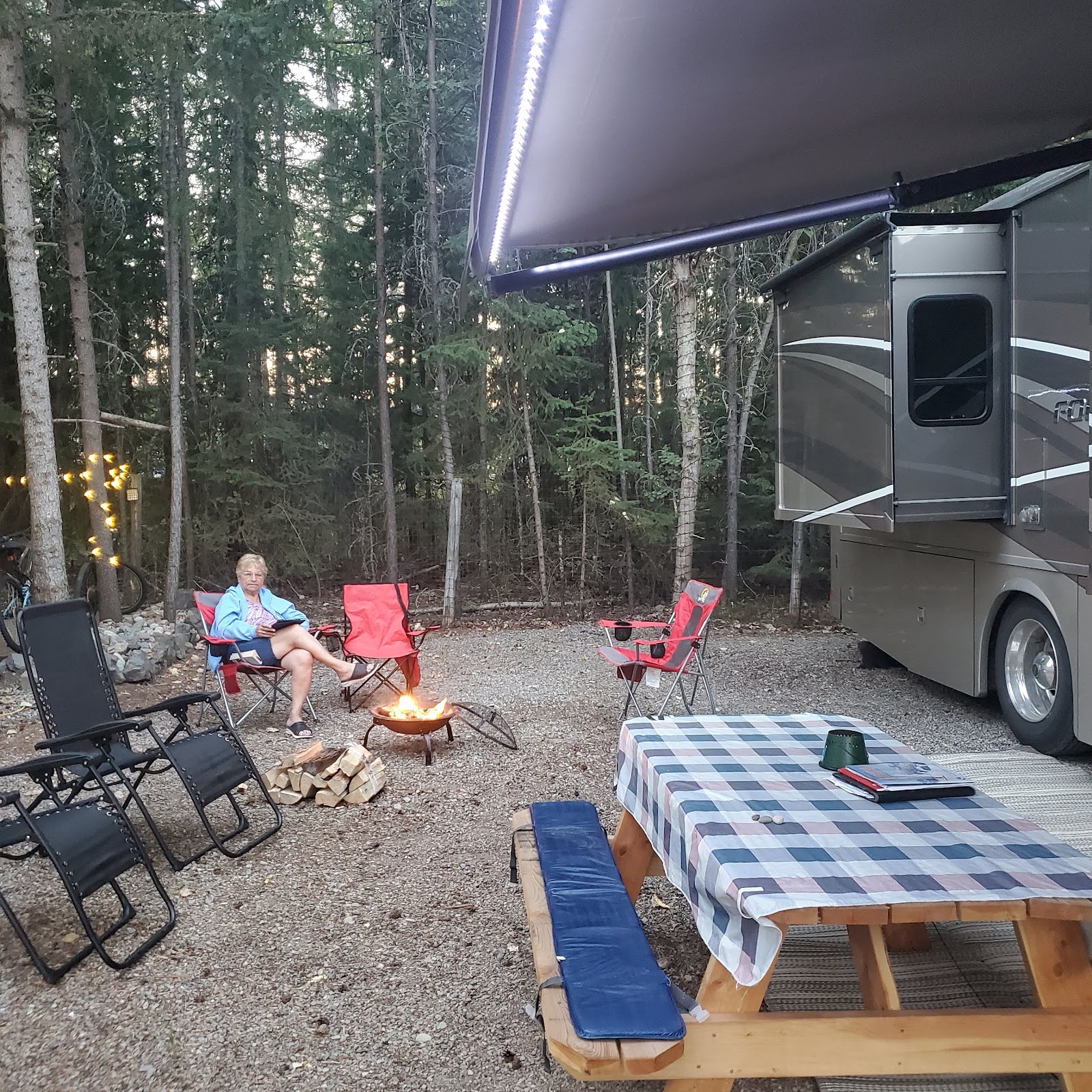 Campground scene in Glacier National Park with an RV, fire pit, and folding chairs around a small blaze.