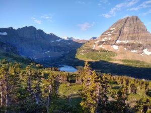 Station 8 overlook in Glacier National Park features a rugged pyramid peak, alpine trees, and a glacial lake bathed in golden light.