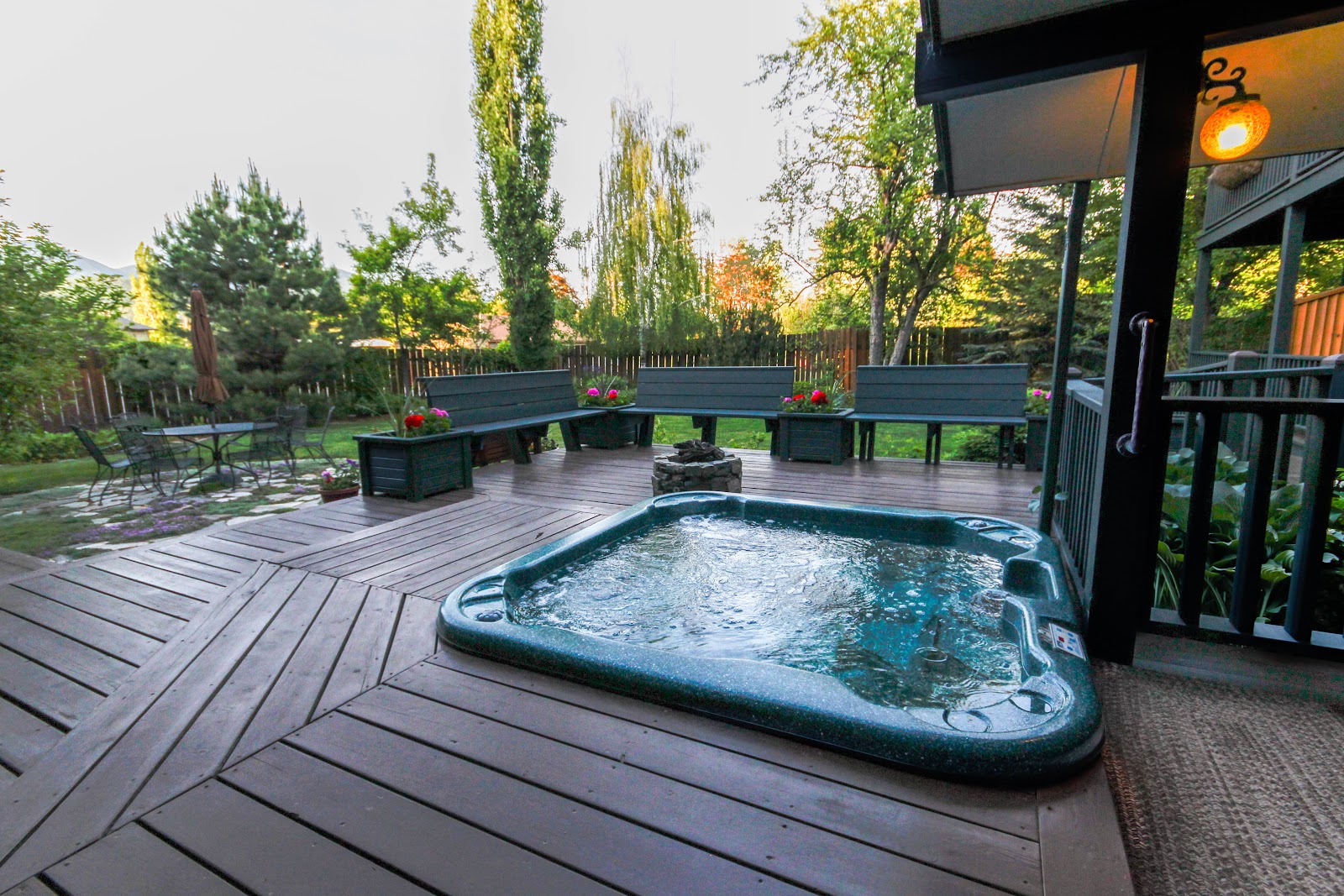 Hot tub on a wooden deck with built-in seating and planters in Glacier National Park lodging backyard.