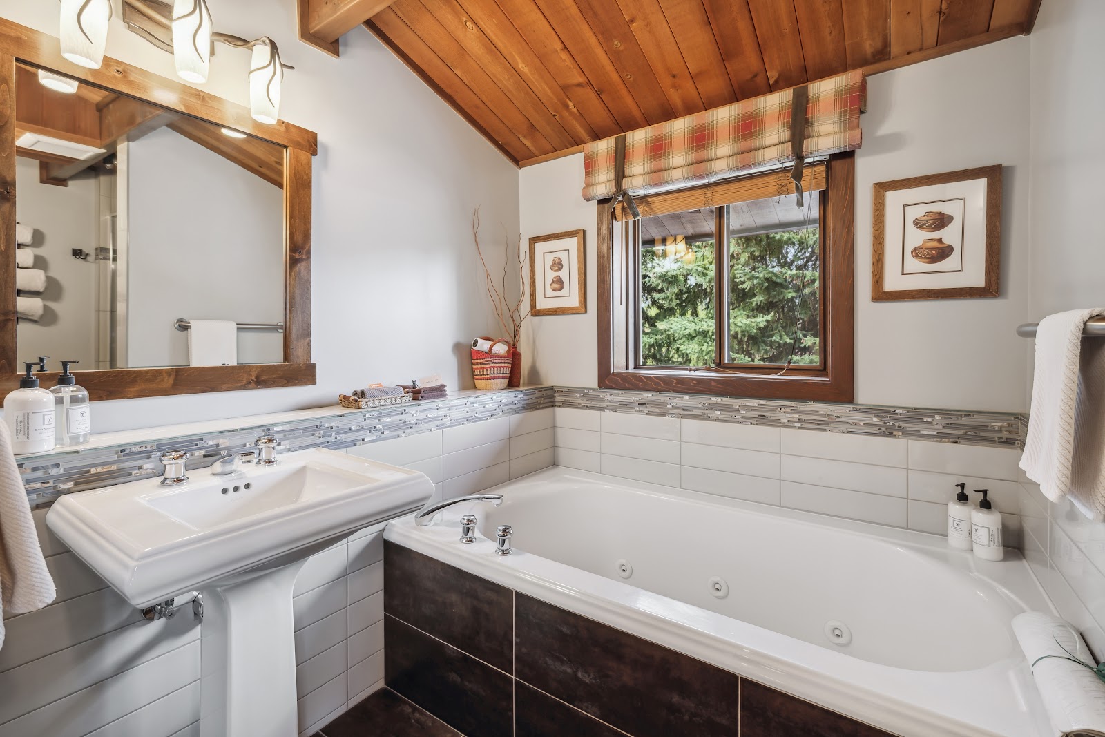 Lodge bathroom in Glacier National Park, featuring a pedestal sink, tub with jets, and a wood-beamed ceiling.