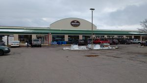 Gift shop exterior in Glacier National Park, showing stacked pallets, carts, and a large parking lot in overcast weather.