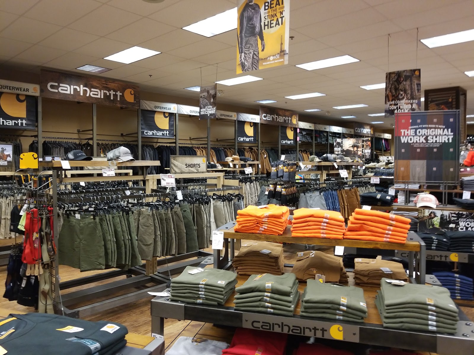 Inside a Glacier National Park gift shop, shoppers browse Carhartt jackets and bright orange sweatshirts on display.