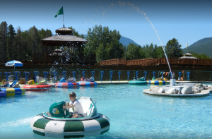 Bumper boats in a water recreation area at Glacier National Park, with a wooden pavilion and mountains in the background.