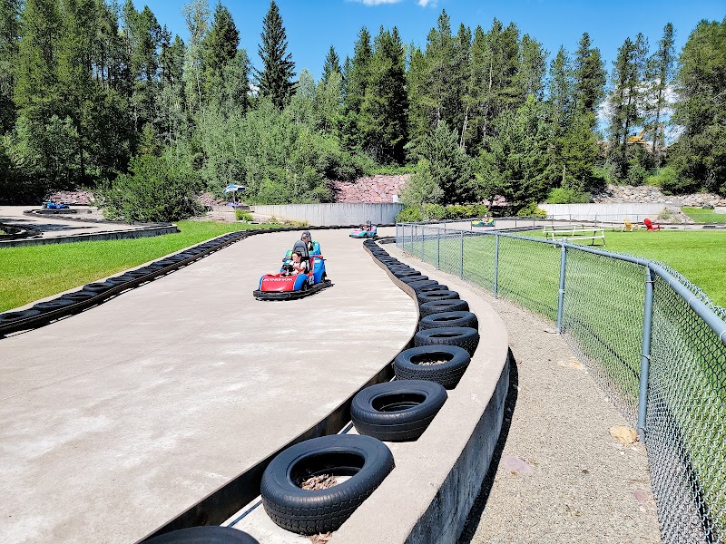 Go-kart track at Glacier National Park with rounded concrete circuit, tire barriers, and pine trees in a sunny setting.