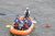 Six rafters wearing helmets and life jackets paddle an orange raft through gray-green rapids in Yellowstone National Park.