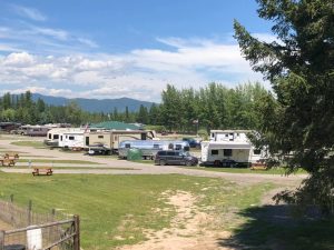 RVs and trailers parked at Whispering Pines RV Park in Glacier National Park amid green fields and tall pines.