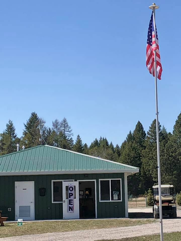 Campground office at Glacier National Park on a sunny day, with an American flag flying beside a green building.