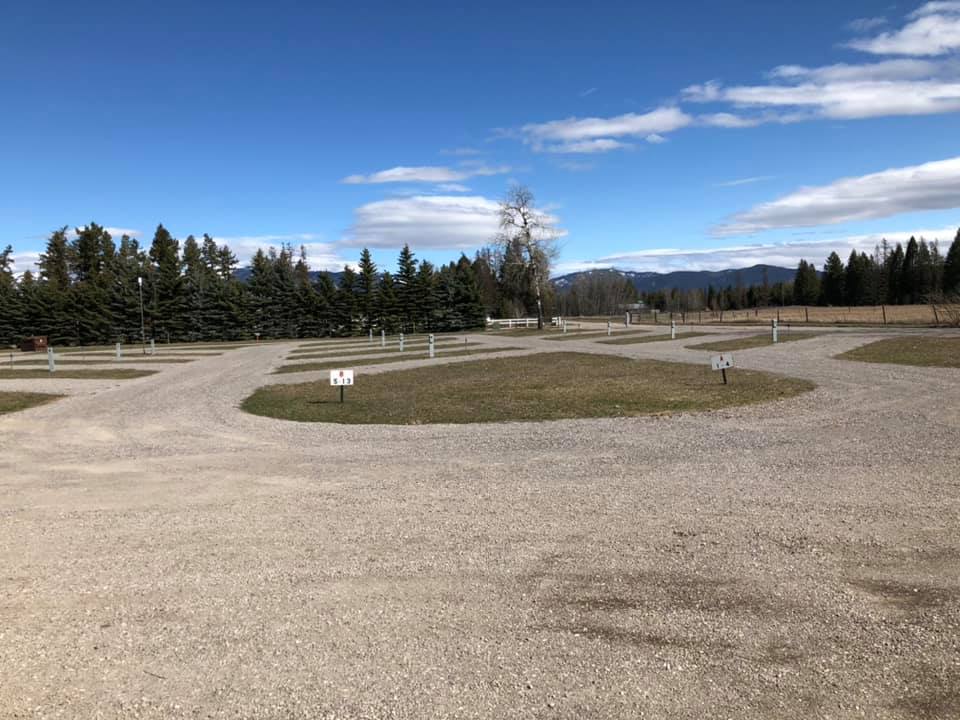 Gravel campground loops and gravel roads wind through Glacier National Park with pine trees and distant mountains under a blue sky.