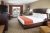 Spacious Yellowstone lodge guest room with a king bed, orange runner, sofa, and work desk in a warm, modern interior.