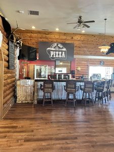 Rustic pizza restaurant interior in Glacier National Park with log walls and a long bar.