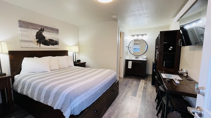 Cozy Yellowstone National Park room with a king bed, striped comforter, nightstands, lamps, eagle art, and a desk.