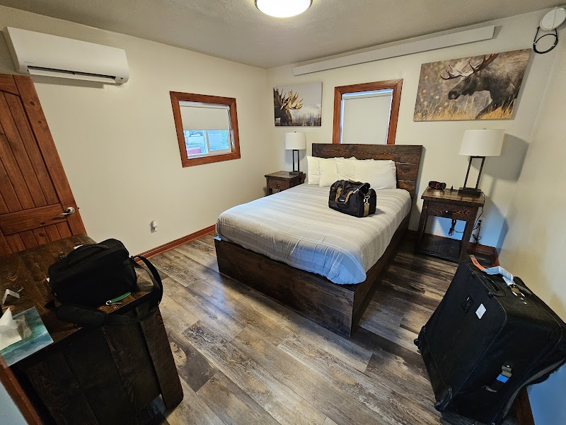 Cozy bedroom with a dark wood bed, two nightstands, elk art, and luggage near small windows in Yellowstone National Park.
