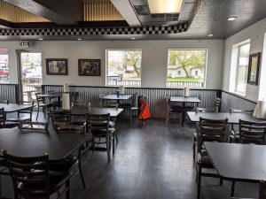 Interior of a casual restaurant in Columbia Falls near Glacier National Park, with dark tables, black chairs, and corrugated metal wainscoting along the walls.