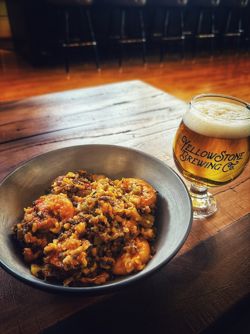 Rustic bar in Yellowstone National Park with a bowl of shrimp and vegetable hash beside a frothy beer on a wooden table.