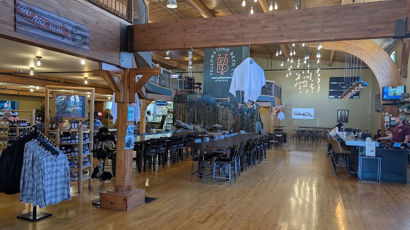 Inside a Yellowstone National Park restaurant with long wooden tables, timber beams, warm lighting, and merchandise shelves.