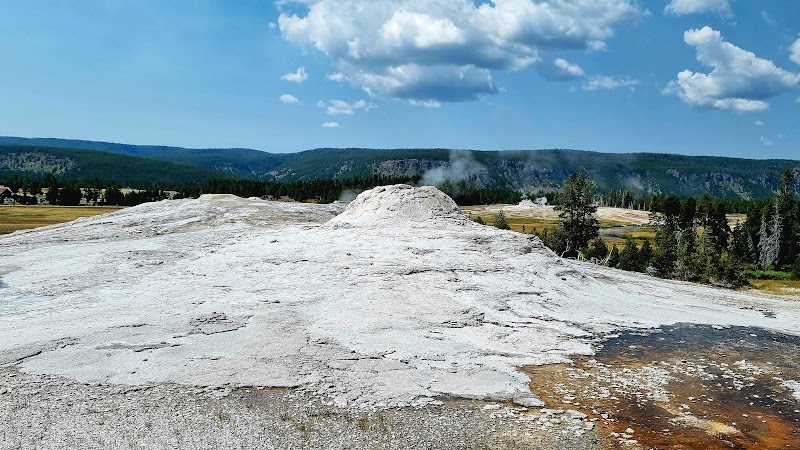 White travertine terrace at Observation Point Trailhead in Yellowstone National Park with distant forest and blue sky.