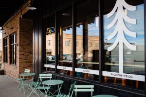 Glacier National Park cafe storefront with mint-green outdoor tables along a brick wall and large windows.