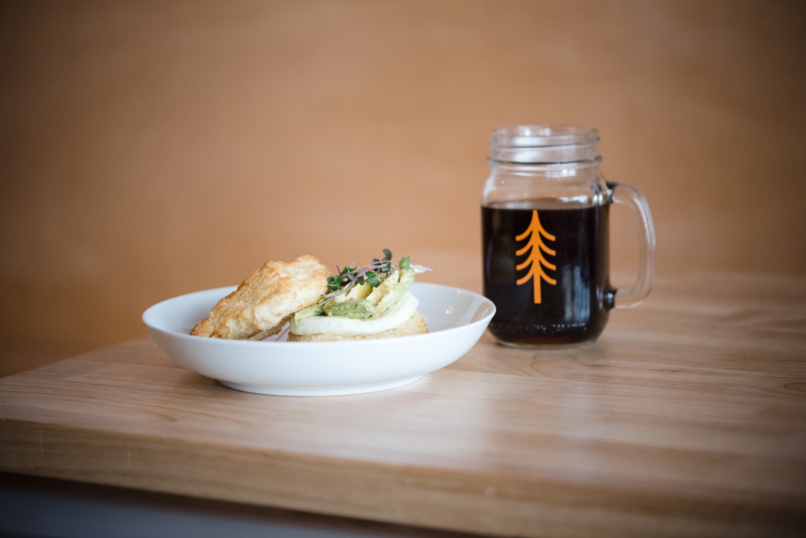 Plate featuring a croissant sandwich with greens and a coffee on a wooden table in Glacier National Park.