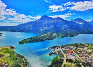 Bear's Hump Trailhead offers a vivid view over Lake McDonald with jagged Glacier peaks rising in the distance, under a blue sky.