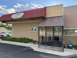 Exterior view of a beige restaurant building in Glacier National Park with a red curved awning and open sign.