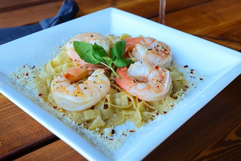 Shrimp on al dente pasta with grated Parmesan and a basil garnish in a square white bowl, Yellowstone National Park.