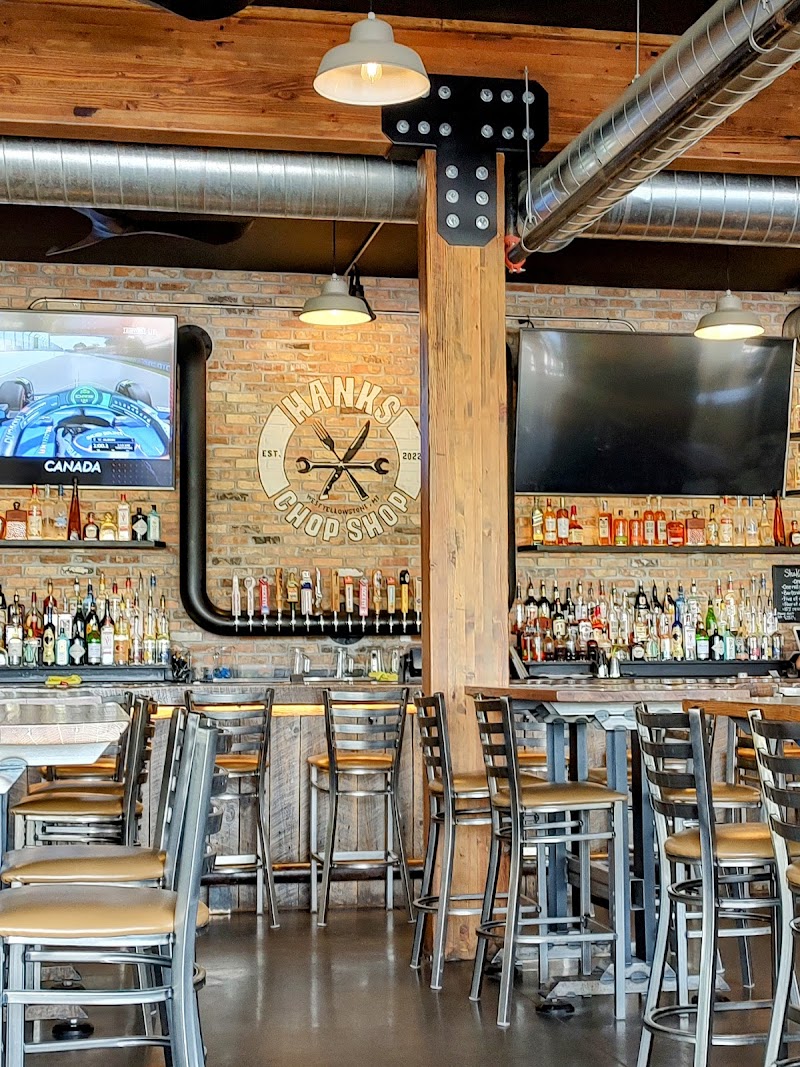 Rustic Yellowstone National Park bar with brick walls, a wooden pillar, metal stools, liquor bottles, TVs, and a racing game on screen.