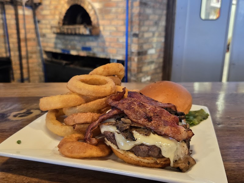 Juicy burger with melted cheese and crispy bacon on a toasted bun, plus a tower of onion rings beside it, set on a plate in Yellowstone National Park.