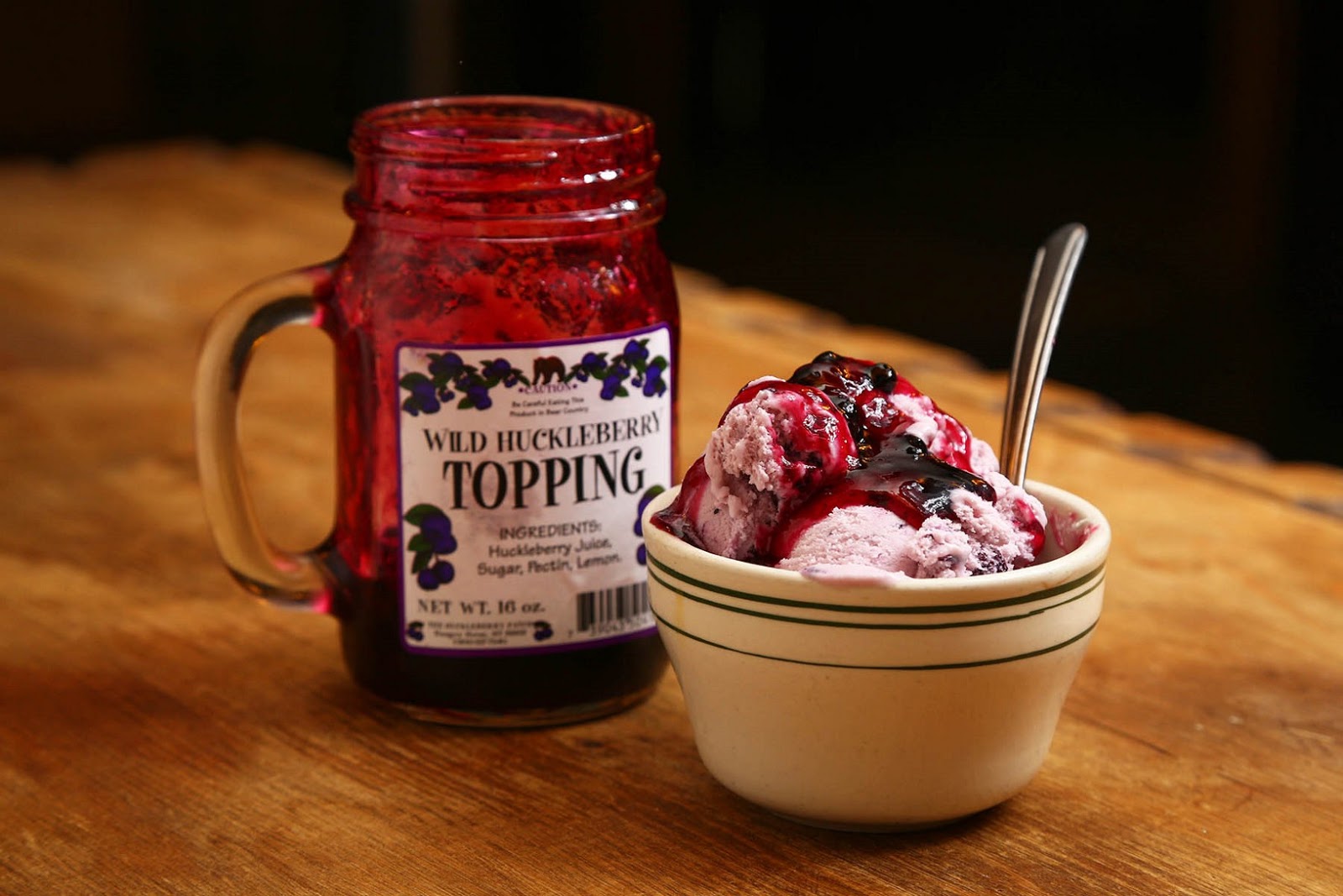 Scoops of pink ice cream topped with wild huckleberry sauce beside a jar of topping in Glacier National Park.