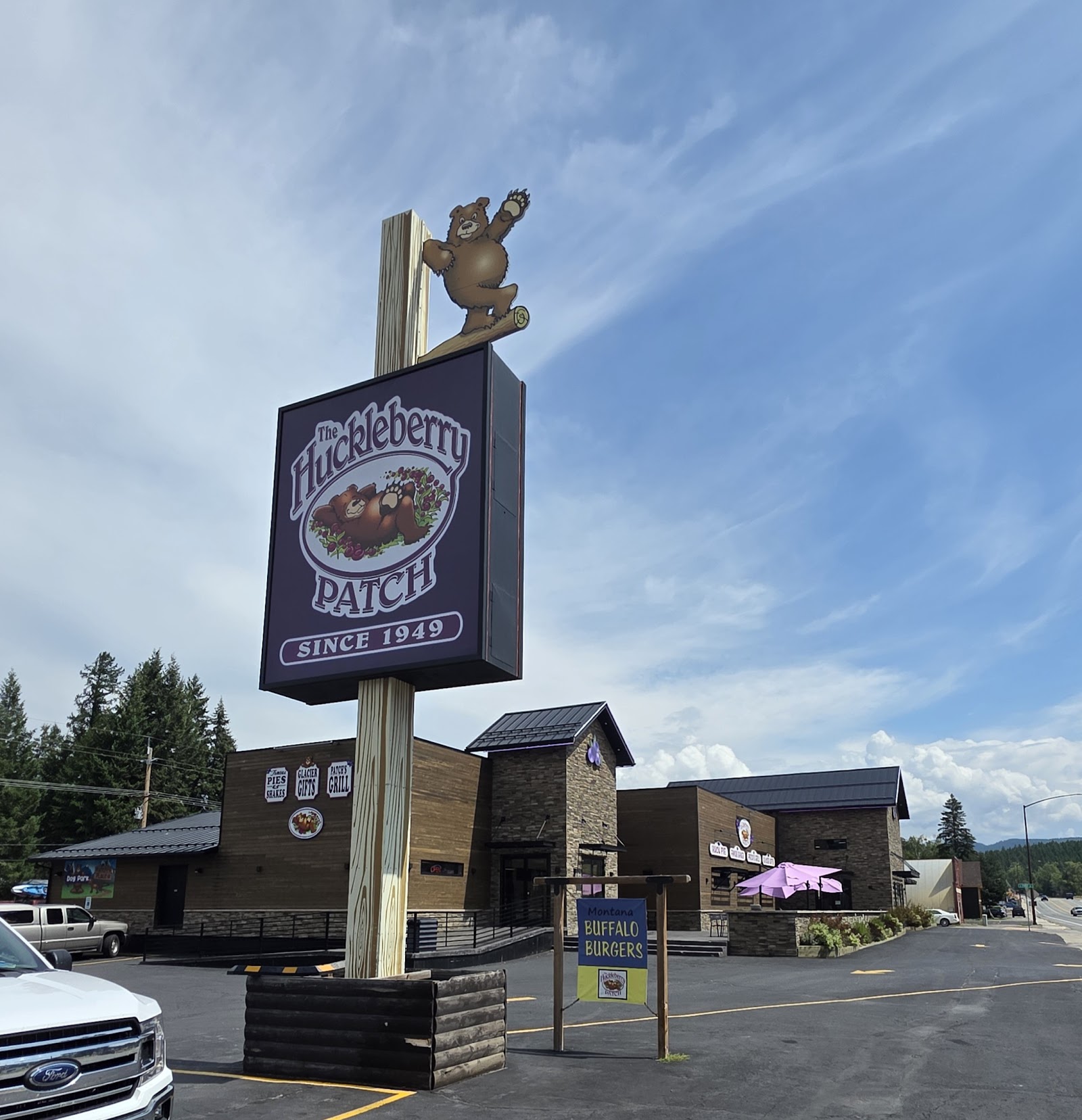 Tall sign featuring a bear statue atop a rustic eatery sign in Glacier National Park, with a clear blue sky.
