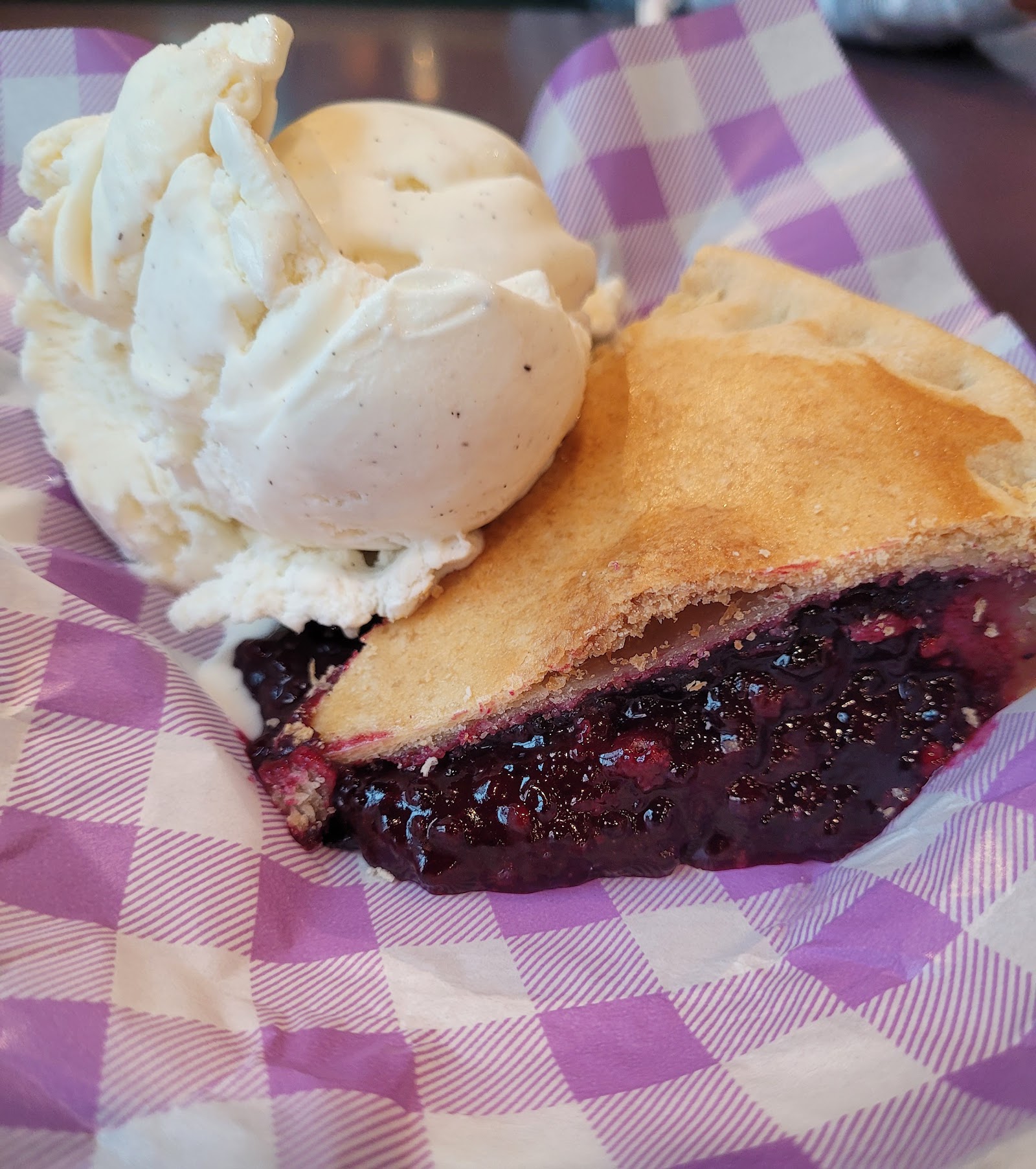 Blueberry pie a la mode with vanilla ice cream served at Glacier National Park, presented on purple checked paper.