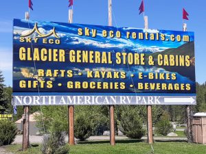 Glacier General Store & Cabins sign at Glacier National Park advertising rentals, kayaks, and gifts near RV park facilities.