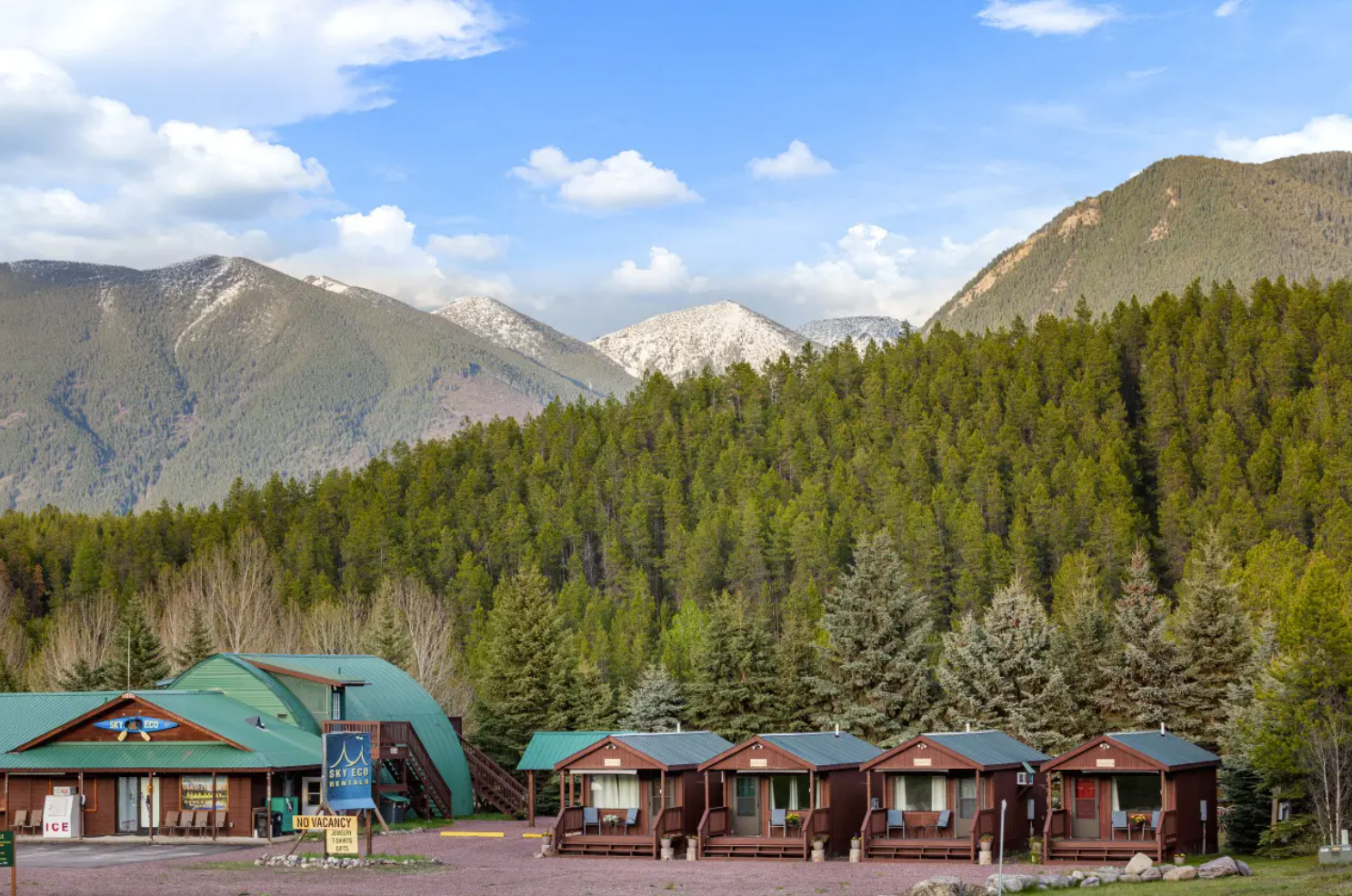 General store and rental cabins sit at the edge of a evergreen forest with snow-dusted mountains in Glacier National Park.