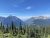Highline Trailhead overlook in Glacier National Park with jagged alpine peaks and evergreen trees under a clear blue sky.