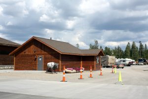 Wooden campground office in Yellowstone National Park with a buffalo statue, orange safety cones, and parked RVs.