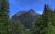 Mount Vaught rises above dense forest in Glacier National Park, jagged rock peaks under a clear blue sky.